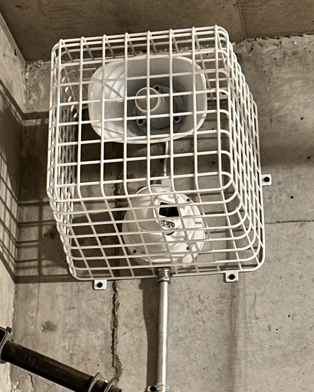 Camera and speaker protected by a wire cage on a concrete wall