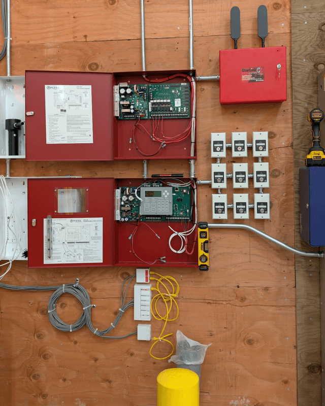 Two fire alarm panels and a cellular communicator on a plywood backboard